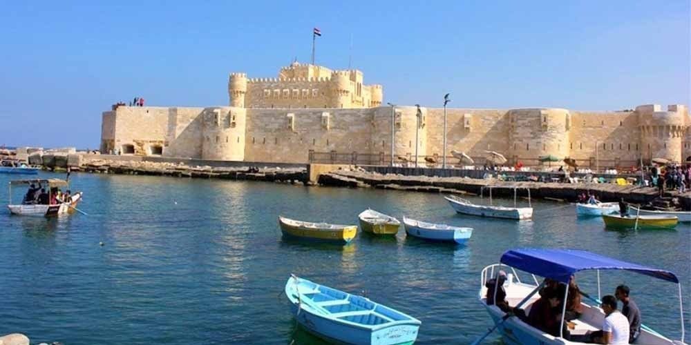 Torres e muralhas da Cidadela de Qaitbay com o mar azul ao fundo.