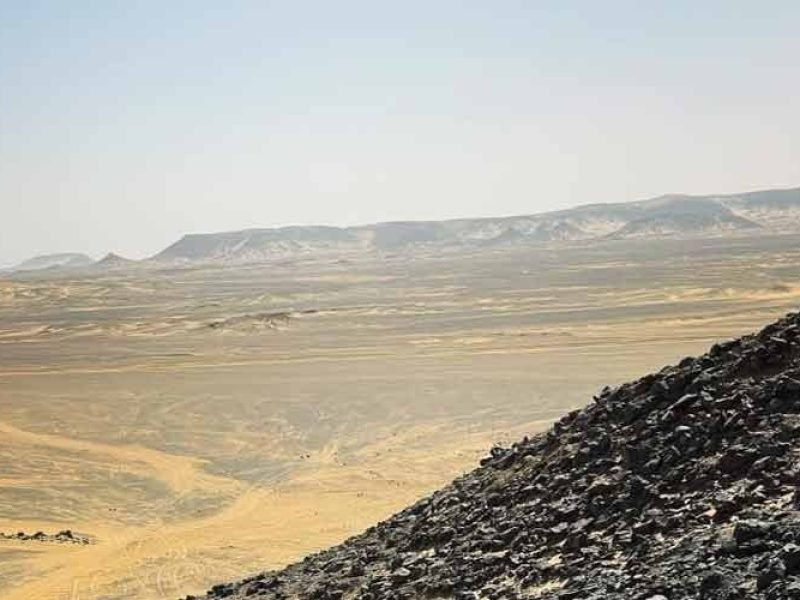 Dunas escuras do Deserto Negro sob um céu azul limpo.