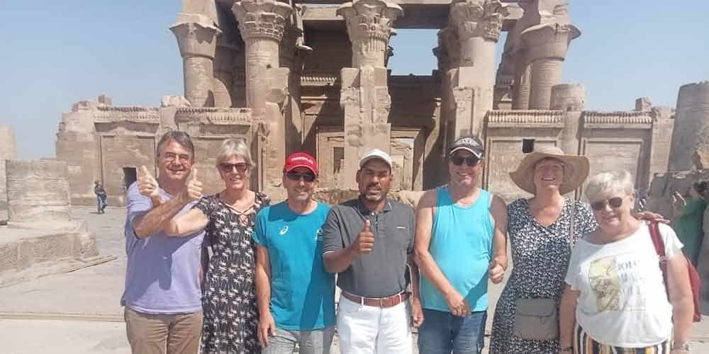 A happy group of tourists posing with their guide in front of an ancient Egyptian temple during their Dahabyia journey.