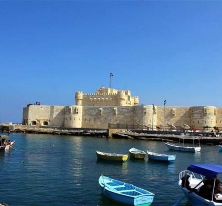 Vue panoramique sur l'eau bleue parsemée de barques colorées devant la forteresse historique, prête pour le spectacle son et lumière de la citadelle de Qaitbay