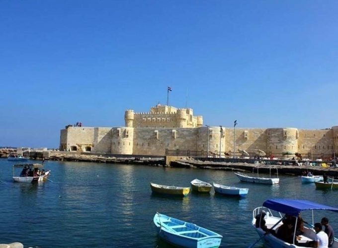 Vue panoramique sur l'eau bleue parsemée de barques colorées devant la forteresse historique, prête pour le spectacle son et lumière de la citadelle de Qaitbay